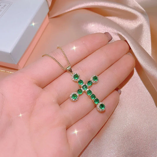 Natural emerald cross necklace with green gemstones set in gold held in hand by MyClosetAid